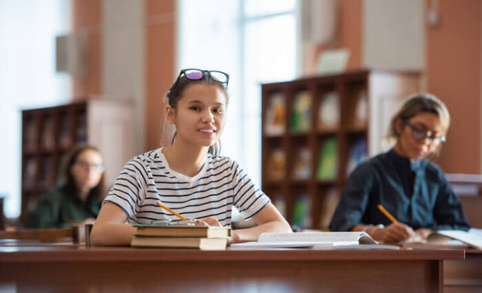 A fast track university prep school student smiling in a library